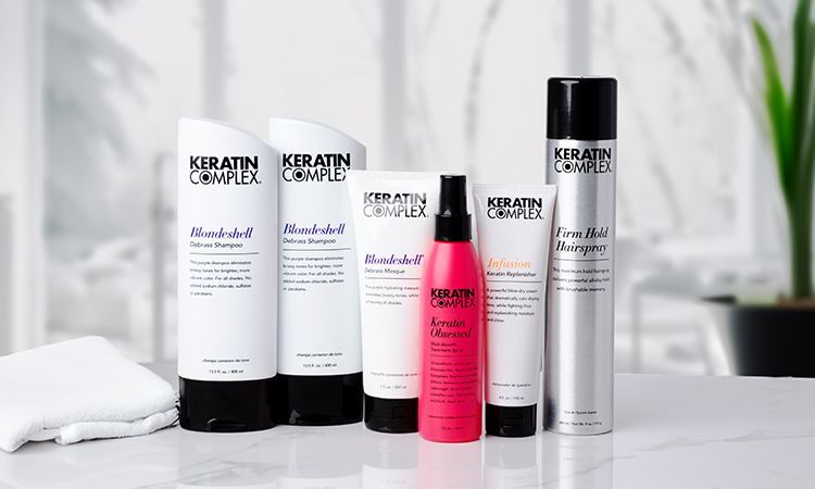 Keratin Complex hair care products, including BlondShell shampoo, conditioner, sprays, and styling items, on a white countertop.