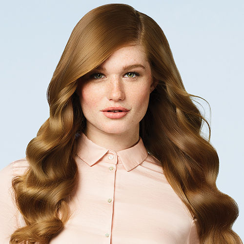 A closeup of a woman who has long curly red hair, she has on a light pink blouse