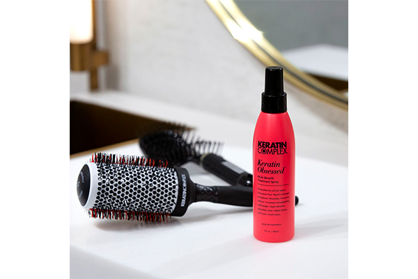 Red bottle of keratin complex next to hair brushes