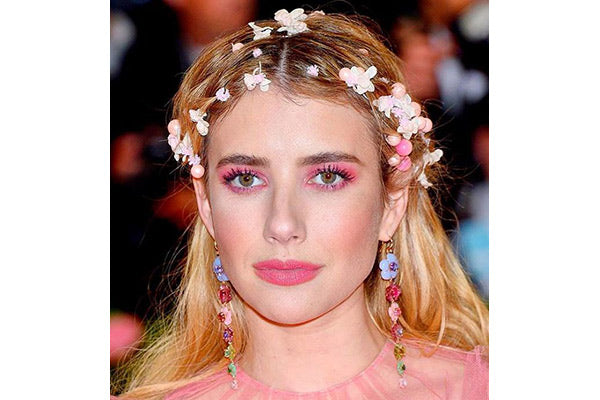 A closeup of a woman, she has long blonde hair with flowers throughout her hair