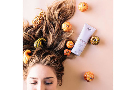A closeup of a woman laying down, her hair is extended, there are small pumpkins near her air and a product bottle