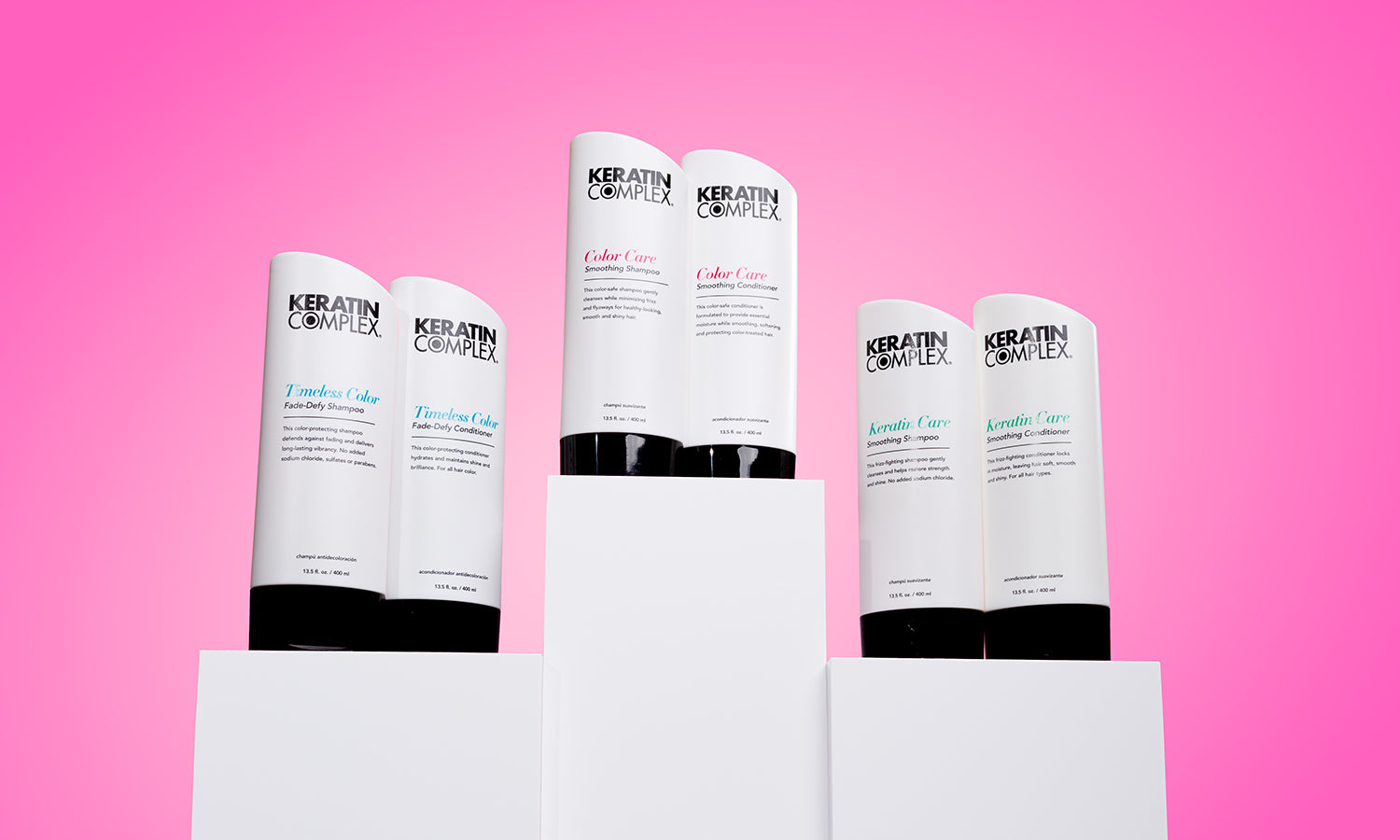 Keratin Complex hair care products displayed on white podiums against a pink background, featuring various bottles from the Timeless Color, Color Care, and Keratin Care collections.