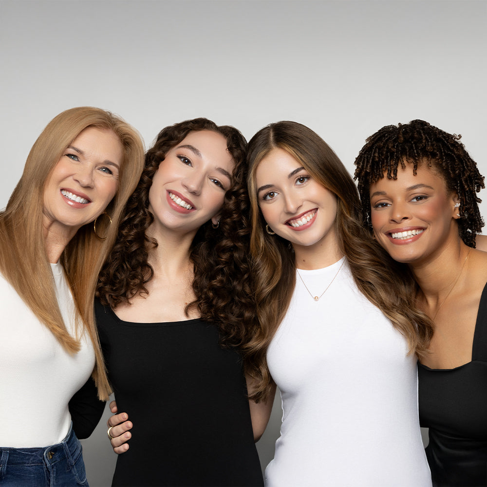 The image features four women with diverse hair textures and styles, all smiling and standing together.