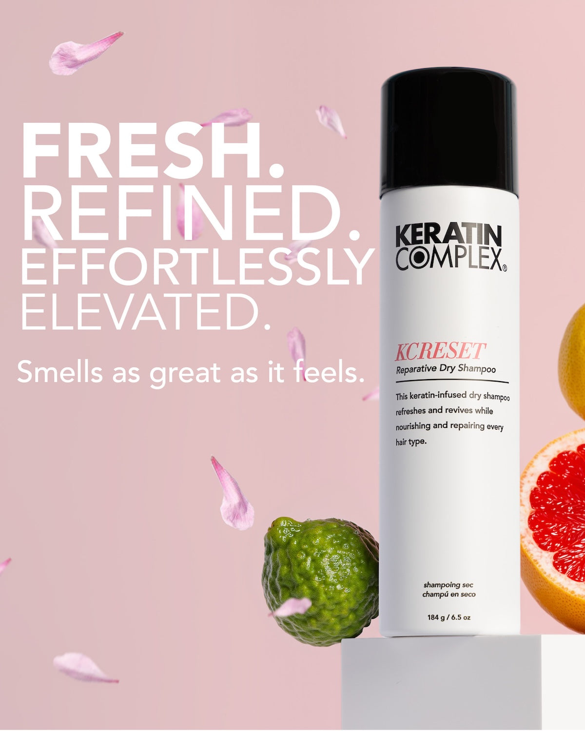 Keratin Complex Kcreset Dry Shampoo in a white can with a black cap, displayed on a pedestal against a pink background with floating citrus slices||FRESH. REFINED. EFFORTLESLY ELEVATED. Smells as great as it feels. 