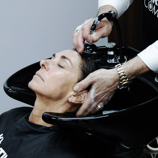 Client receiving a relaxing hair wash at a salon, with close-up focus on the stylist’s hands and the washing process.