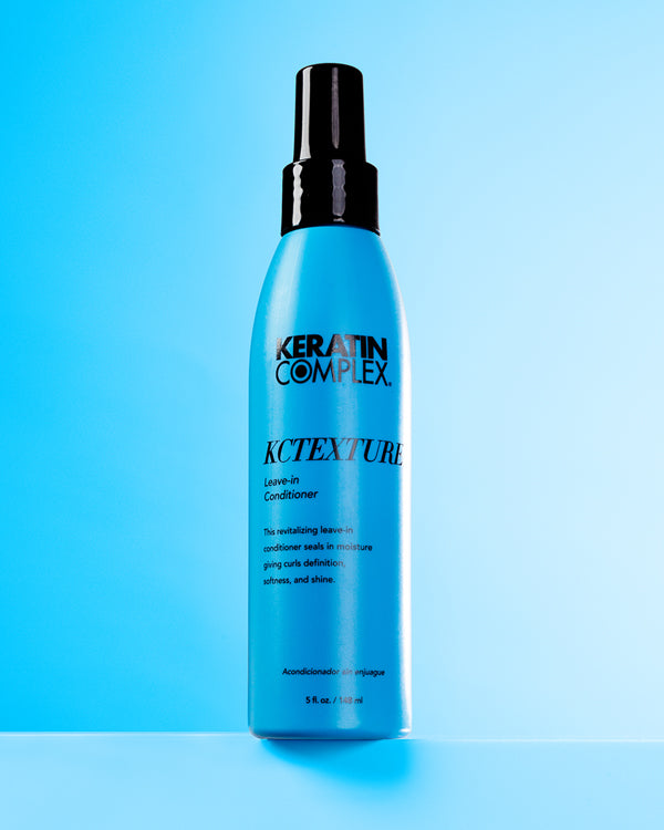 A blue bottle of KCTEXTURE Leave-In Conditioner on a blue background, emphasizing its moisturizing and curl-enhancing properties.