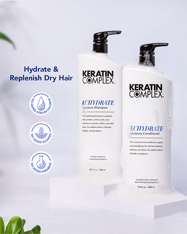 Two bottles of Keratin Complex KCHYDRATE Moisture Shampoo and Moisture Conditioner, are shown with white soap suds around them. Icons highlight that the products contain no added sodium chloride, no added sulfates, and no added parabens. ｜Hydrate & Replenish Dry Hair, no added sodium chloride, no added sulfates, and no added parabens.｜