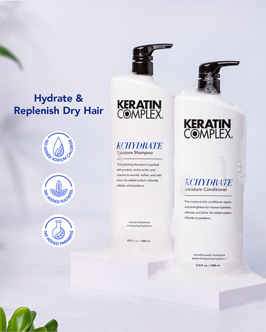 Two bottles of Keratin Complex KCHYDRATE Moisture Shampoo and Moisture Conditioner, are shown with white soap suds around them. Icons highlight that the products contain no added sodium chloride, no added sulfates, and no added parabens. ｜Hydrate & Replenish Dry Hair, no added sodium chloride, no added sulfates, and no added parabens.｜