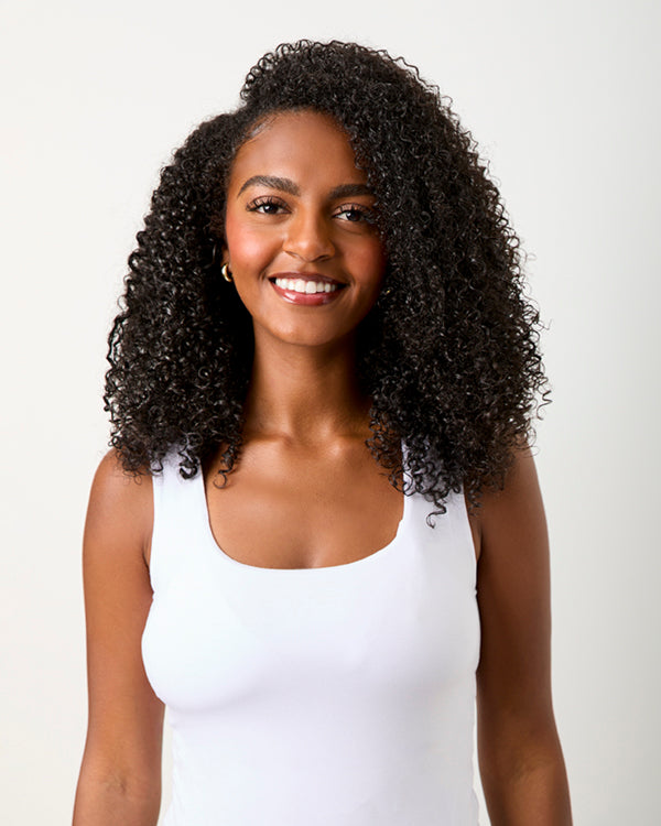 A smiling woman with voluminous, curly hair after using KCHYDRATE and Vanilla Bean deep conditioner.