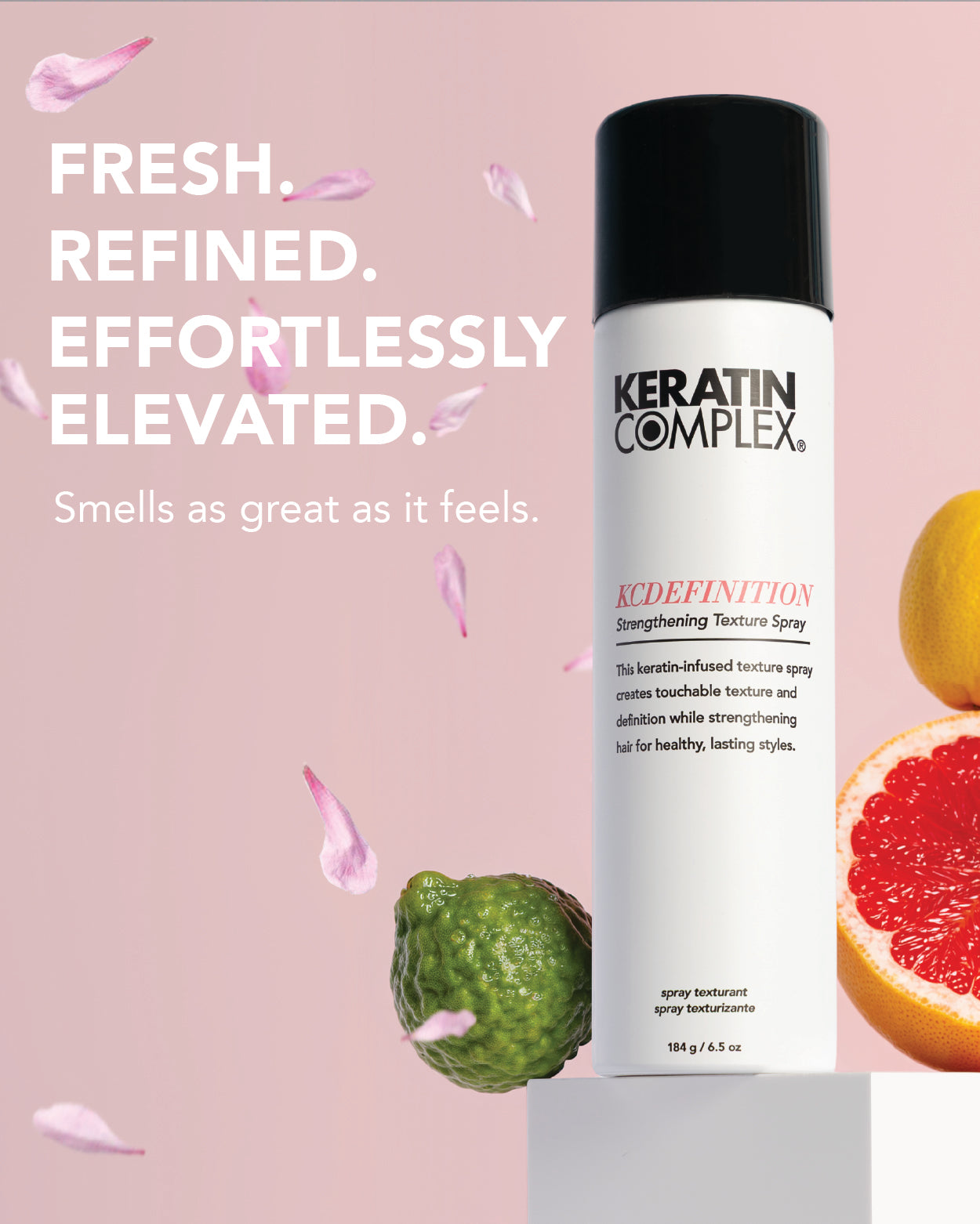 A bottle of Keratin Complex KCDEFINITION  against a pink background with decorative text and fruit/flower props. ||FRESH. REFINED. EFFORTLESSLY ELEVATED. Smells as great as it feels. 