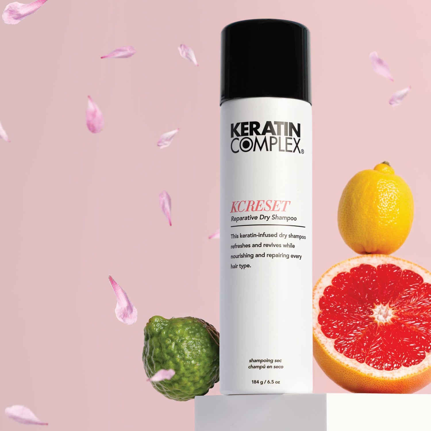 Keratin Complex KCREST, styled on a pedestal with a pink background and citrus fruits including a lemon, grapefruit, and a lime, with petals floating around.